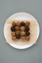 Oatmeal energy balls with nuts, dates, pumpkin seeds, cranberries, prunes and tangerines on a white plate on baking paper on on a gray background. Horizontal orientation.