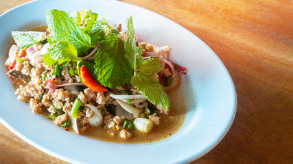 Spicy Thai food Minced Pork Salad serve on wooden table.