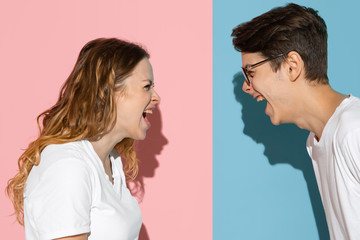 Screaming angry on each other. Young and happy man and woman in casual clothes on pink, blue bicolored background. Concept of human emotions, facial expession, relations, ad. Beautiful caucasian