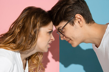 Angry face to face. Young and happy man and woman in casual clothes on pink, blue bicolored background. Concept of human emotions, facial expession, relations, ad. Beautiful caucasian couple.