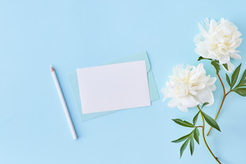 Obraz na płótnie Canvas Mockup wedding invitation and envelope with white peonies on a blue background