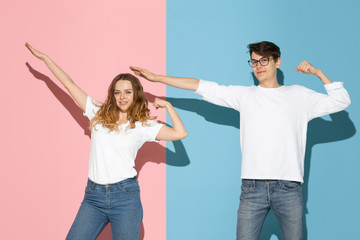 Obraz premium Success winner gesture. Young and happy man and woman in casual clothes on pink, blue bicolored background. Concept of human emotions, facial expession, relations, ad. Beautiful caucasian couple.