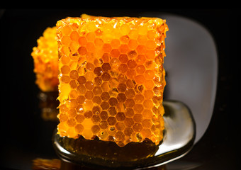 Honey close-up. Amber sweet honey in honeycomb. Square cut piece of honeycomb with honey on a black...