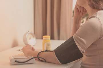 Mature woman checking her blood pressure with digital tonometer at home