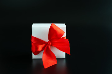 White gift box with big red bow on black background with copy space for your text. Holiday concept. Minimalism style composition.