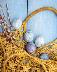 Painted blue Easter eggs in a wicker bag on a blue wooden background.