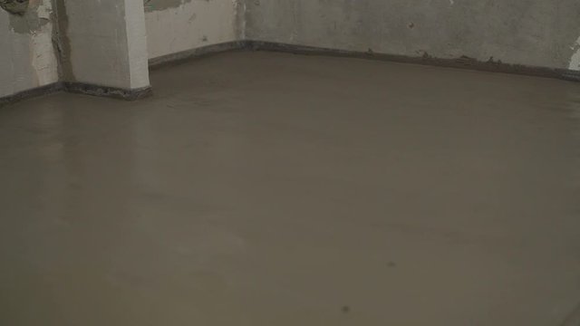 Leveling the floor with a long spatula. Builder levels a laid floor. Floor laying at home. The builder is laying concrete floor in the apartment.