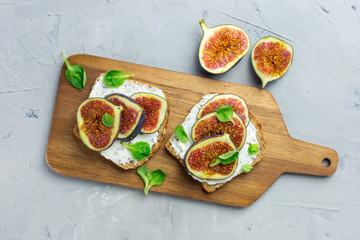 Two Sandwiches with cream cheese, figs, honey and leaves salad served on the wooden rustic cutting board on gray background. Healthy food concept. Top view