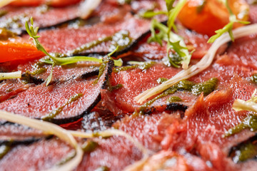 Closeup Beef carpaccio with pesto sauce and tomatoes on black table. Restaurant menu, natural and organic food concept.