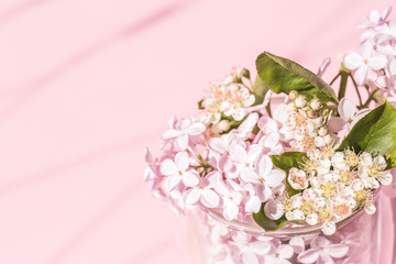 Assorted lilac and spring flowers in bloom in glass vase on pink background with copy space and shadow. Birthday celebration or wedding invitation card. Spring summer concept.