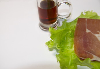  On a white background is a glass of alcohol, a green leaf of lettuce, meat, boiled eggs.