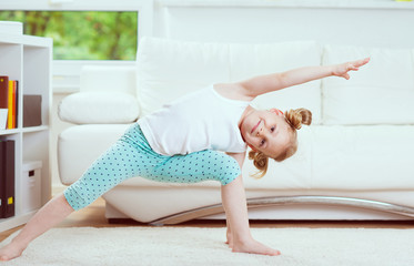 Cute little child girl making morning exercises at home