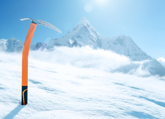 Der orangefarbene EISPICKEL für Höhenbergsteiger. Es ragt im Schnee auf dem Schneeeisfeld mit dem Gipfel Ama Dablam (6812 m) heraus, der mit Wolkenhintergrund bedeckt ist. Urlaubskonzept für extreme Menschen
