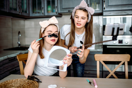 Two teenage girls with beautiful smile reading good news on mobile phone. Beauty blog for social networks. The first cosmetics for a teenager. Video recording at home