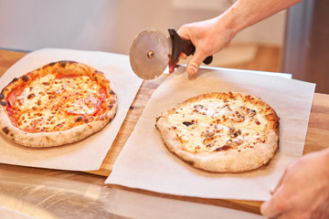 Italian kitchen and cooking concept. Chief with a pizza cutter cutting pizza to pieces at Neapolitan pizzeria.