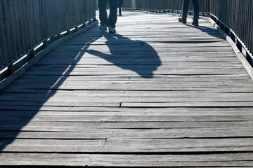 shadows of a man and woman walking on an old wooden bridge