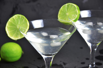 Two glasses of martini with lime on a black background. Two glasses of martini cocktail in a bar