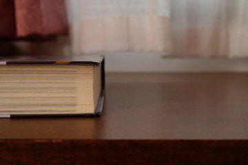 Close up of Thick old book that place on a table near to the window