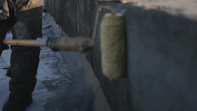 the roofer applies glue to the parapet with a roller. Winter in the North on a nice Sunny day