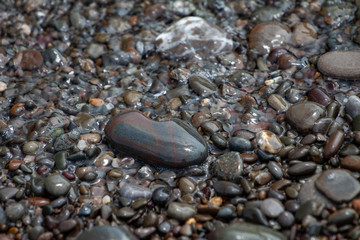 sea pebbles colored granite on the beach background stones. The shore of the beach with sand and pebbles washed by the waves of the sea. © mironovm