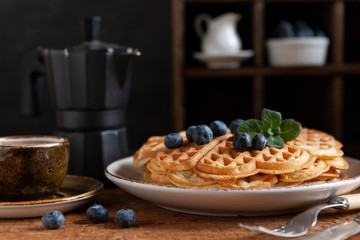 Close-up of soft Viennese waffles with blueberries, a cup of coffee and a coffee pot