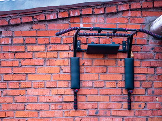 A sports horizontal bar mounted on a red brick wall of a house. Outdoor gymnastics workout equipment