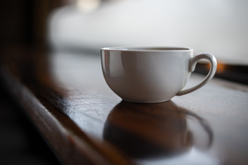 The white ceramic coffee cup with coaster is placed on a brown wooden base on the back, naturally a blurred background.