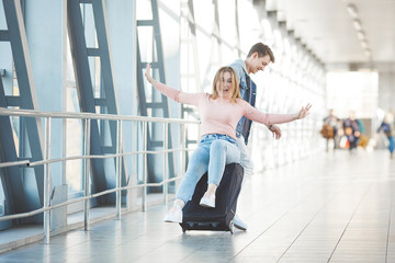 Fototapeta na wymiar Happy young couple at the airport terminal having fun while waiting for their flight. Two people man and woman going to trip.