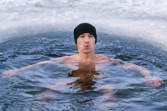A man in a hat plunges into ice water in winter and takes his breath away