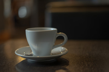 The white ceramic coffee cup with coaster is placed on a brown wooden base on the back, naturally a blurred background.