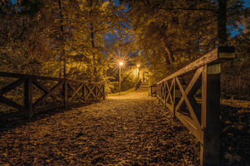 Autumn in the city park. A night shot with a wooden bridge, a street lamp and an old city wall. Concept: cityscape and urban views