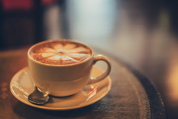 A white cup of coffee with spoon and saucer on a wooden table and luxury vintage. a blur of bokeh 