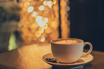 Obraz premium A white cup of coffee with spoon and saucer on a wooden table and luxury vintage. a blur of bokeh 