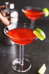 Red cocktail with lime in Martini glass on a table.