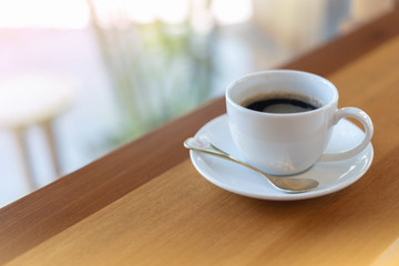 The white ceramic coffee cup with coaster is placed on a brown wooden base on the back, naturally a blurred background.