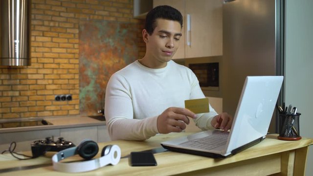 Young man shopping online, paying with credit card, goods show up in stop motion