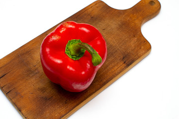 One bright red raw bell pepper with green tail on a wooden board, closeup isolated white background