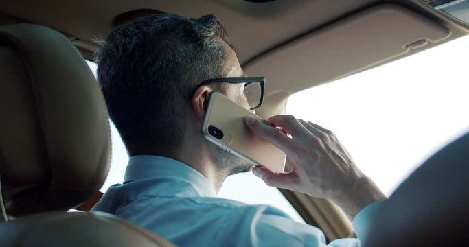 Rear of the Caucasian man in business style and glasses driving a car and talkig on the mobile phone. View rom the back sit. Close up.