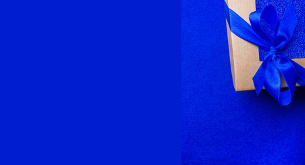 festive gift wrapped present box with blue satin bow close up isolated on trendy blue background