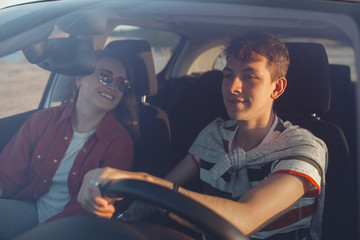 Pretty young couple driving the car at sea shore. Woman and man having fun at the trip. People traveling on automobile.