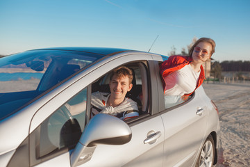 Pretty young couple driving the car at sea shore. Woman and man having fun at the trip. People traveling on automobile.