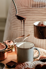 Beautiful young girl in beige apron is preparing delicious organic hot chocolate in old vintage ladle. Soft daylight, lifestyle photography, process of tasty drink creation. Close up
