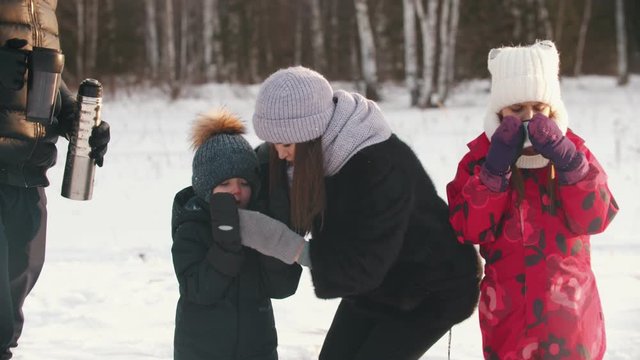 Family drinking hot drinks from the termos in nature while winter time