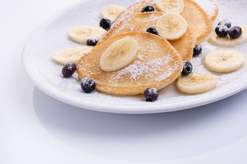 pancakes with banana and blueberries on a white plate, tasty and beautiful on a white background