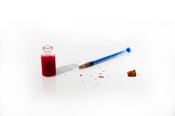 Medicine syringe and red drops from glass tube on white table. Virus abstract photo.