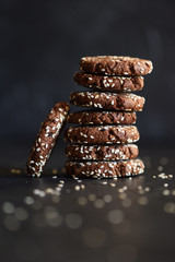 Vegan gluten free chocolate cookies with white and black sesame seeds on black background copy space