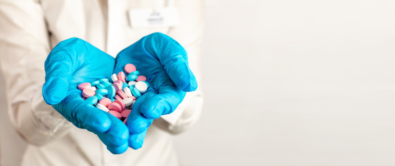 Close-up the doctors hands in blue medical gloves are stretched forward and hold pills, medicine, vitamins and antibiotics for the treatment of health on light background, copy space.