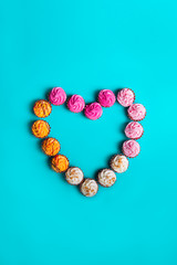 Top view Allsorts chocolate Sweets with multicolored cream filling arranged in heart shape on light blue background. Happy Valentine's day. Love festive concept. Flat lay. Vertical card. Copy space.