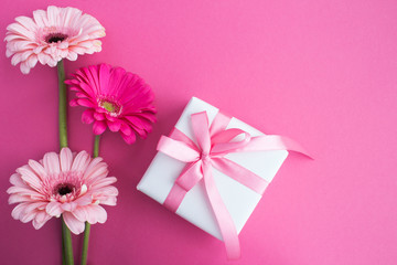 Gift with pink bow and pink flowers on the pink background.Top view.Copy space.