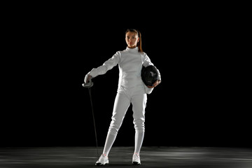 Confident. Teen girl in fencing costume with sword in hand isolated on black background. Young...